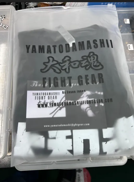 Custom-printed clear poly mailer with black text and graphics, resting on a plastic bin. Text reads, 'YAMATODAMASHII 精神 THE FIGHT GEAR by Enson Inoue www.yamatodamashifightgear.com'.