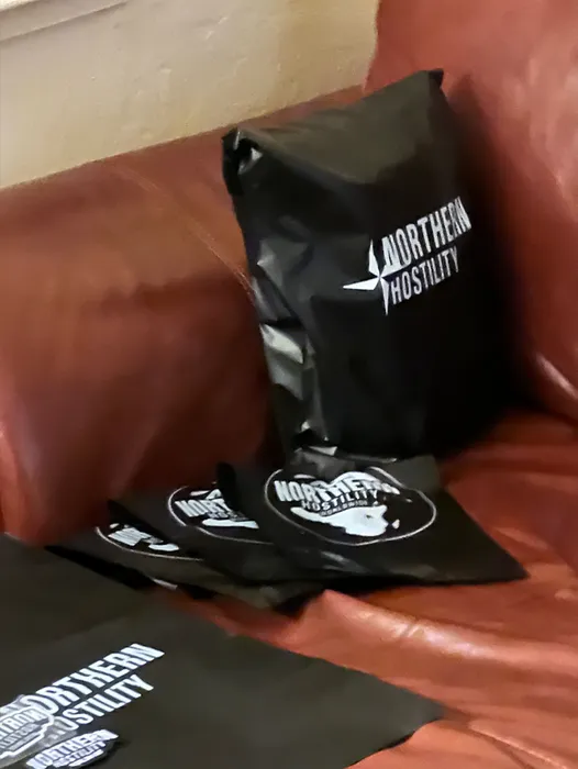 Custom black poly mailers with 'NORTHERN HOSPITALITY' text are displayed, resting on a brown leather surface, likely promoting brand packaging.
